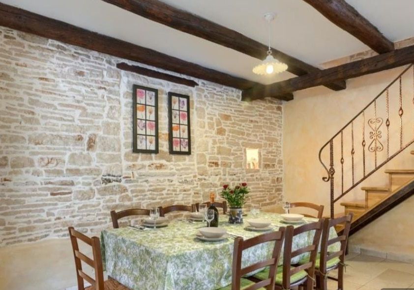 The dining room laid for a meal beneath wooden ceiling beams, with an exposed stone wall and a staircase.