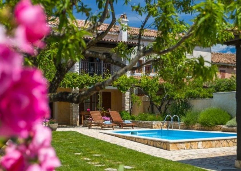 The private pool at Casa Paulina with sun loungers on the lawn and the stone house behind, framed by pink bougainvillea.